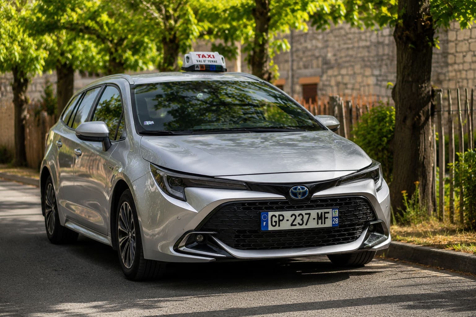 L'Amotaxi, Toyota Corolla grise avec son lumineux Val d'Yerre, dans une rue arborée au soleil